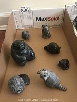 Seven soapstone animal figurines arranged in a box including raccoon, beaver, turtle, duck, frog, fish, and one small figure.