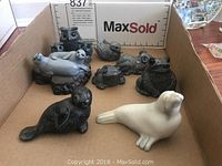 View of seven soapstone animal figurines including seals, frogs, a turtle, and an owl trio inside a cardboard box
