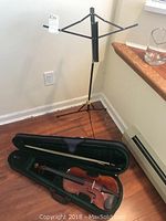 Full view of the violin in open case with bow, music stand behind