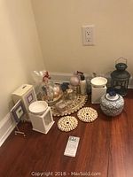 Wide angle view showing assortment of candles, soaps, shell coasters, lantern, ceramic urn and oil burner on wooden floor next to wall outlet