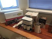Three kitchen appliances displayed on countertop including Philips Cafe Duo coffee maker, Hamilton Beach electric knife set in box, and Philips coffee grinder box.