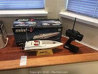 Mini-V speedboat model on yellow stand alongside original box and remote control on wooden surface.