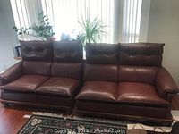 Two brown leather sofas with wooden frame accents, shown side by side in living room.