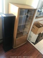Full view of the stereo stand and adjacent black VHS holder in a room with hardwood flooring and a window.