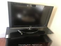 Front view of Samsung 40 inch TV on black glass top TV stand with remote on stand.