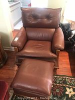 Full view of brown leather chair and matching ottoman on hardwood floor with a patterned rug.