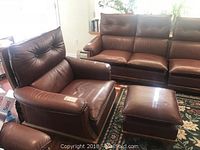 Brown leather armchair matched with ottoman, showing overall look and setting with carpet underneath.