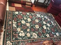 Large green floral area rug, laid on hardwood floor with furniture around.