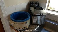Waring Pro deep fryer and Rival crock pot slow cooker on kitchen counter by sink.