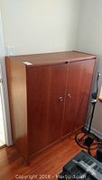 Front view of wooden cabinet showing two doors with chrome or metallic round handles, medium brown wood finish.