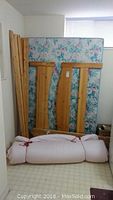 Wooden headboard and footboard leaning against a floral-pattern mattress with a rolled white bedding piece in front.