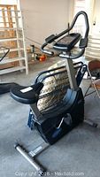 Full view of black Universal Fitness stationary exercise bike with cushioned seat in storage area with other items nearby