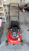 Front view of red push lawn mower with black handlebar and rear bag, showing overall condition and design.