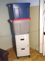 Full view of two drawer beige metal file cabinet with two large Rubbermaid storage containers stacked on top.