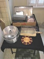 Top-down view of bakeware lot showing sheet pans, bread pans, cooling racks, and trivet on black cloth