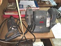 Photo showing the Black & Decker bench grinder next to the Milwaukee electric drill on a wooden table, including their power cords.