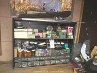 Full view of black three-shelf metal counter unit loaded with multiple compartments of assorted fasteners, clips, sandpapers, and various small hardware items organized in drawers, bottles, and boxes.