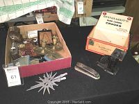 Lot overview showing antique portable gas light, brass candlesticks, vintage scale, stapler, pack of crooks, and various small items in a box.