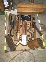 Overhead view of box containing assortment of wooden and metal hand tools: planes, mallet, clamp, drill, brush