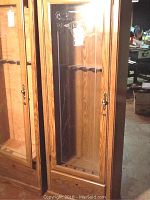 Full front view of the wooden gun cabinet showing glass front door and lock mechanisms.