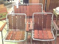 Aluminum framed redwood lawn bench and two folding lawn chairs have slatted redwood seats and backrests with metal armrests and frame
