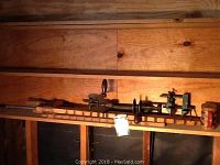 Photo of antique woodworking tools arranged on a wooden shelf showing long wooden clamps and a hand drill press with wooden handle.