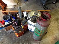 Overview of metal containers including gas cans and sprayer, showing condition and brand labels.