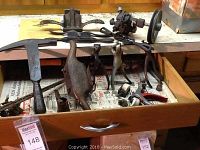 Drawer open showing assortment of hand tools including an axe, draw knives, small clamps, and metal parts.
