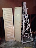 Two wooden shutters positioned upright beside a wooden decorative lawn tower, showing full height and general condition of items.