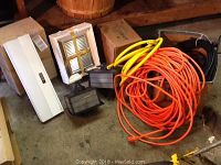 Overview of two exterior house lights, under cabinet mount light in box, Nutone exhaust fan in box, and multiple outdoor extension cords coiled on floor.