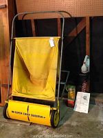 Yellow Super Chief push lawn sweeper with metal frame and collection bag, shown in garage