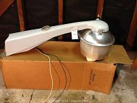 General Electric commercial outdoor security light resting on a box, showing the entire fixture lengthwise with visible wires and mounting bracket.