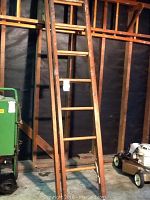 Both sections of the wooden extension ladder leaning against a wall in a garage or workshop space.