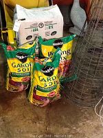 Full view of two Miracle-Gro Garden Soil bags, one Miracle-Gro Potting Mix bag, Premier Peat Moss bag, and tomato cages on floor.