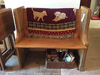 Front view of the oak wooden deacons bench with the maroon blanket draped over the backrest. The bench is wide with armrests and a flat seat.