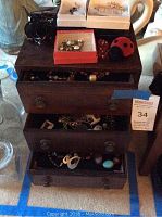 Wooden dark finish 3 drawer jewelry box with various jewelry items around and inside open drawers.