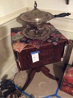 Full view of wooden side table with two drawers, holding the silver-tone serving dish on top, showing the cloth beneath and overall shape.