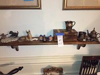 Wooden wall-mounted shelf holding decorative items including animal figurines, wooden box, and metal pitcher and teapot.