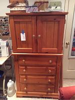 Front view of wooden storage cabinet with four drawers at bottom and two doors at top, showing wood grain and knob handles.
