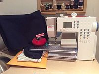 Sewing machine on tabletop with black cover folded behind, manual and accessories at front