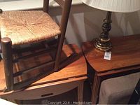 Wooden rocking chair with woven seat placed on wooden side tables, showing furniture details and condition.