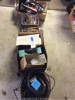 Top-down photo showing multiple boxes containing various hand tools such as chisels, screwdrivers, and drill accessories, also includes electrical cords and hardware items.