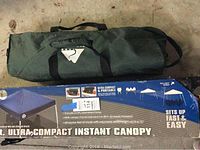 Green carrying bag with black straps for the canopy tent and packaging box showing Ultra Compact Instant Canopy with setup images and features.