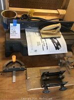 Jointer planer top view showing black body, power cord, user manual, and two adjustable fences with orange handles on the work surface.