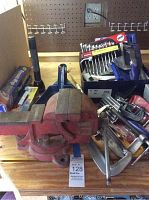 Full display of bench vice in front with box of tools, wrench set and clamps around it on workbench