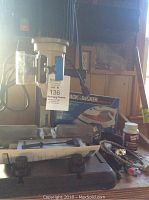 Wood River mortising machine with attached power cord, manual, and safety shield, surrounded by miscellaneous accessories including boxed Black & Decker iron.