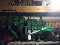 Photo showing two green Scott spreaders, a small garden sprinkler, and a Weedeater string trimmer stacked in a storage area.
