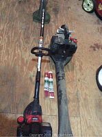 Both the Craftsman blower and Troybilt Weedeater laid out on wooden surface with two tubes of red replacement pre-cut line refills.