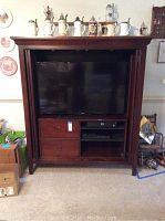 Full front view of wooden TV console with TV inside and decorative items above.