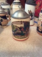 Photo showing front of a cream-colored lithophane beer stein with a romantic countryside scene and German text near base, with pewter lid